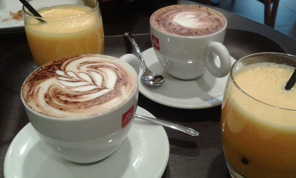 Two capuccino in a white cup and two orange juice in a glass